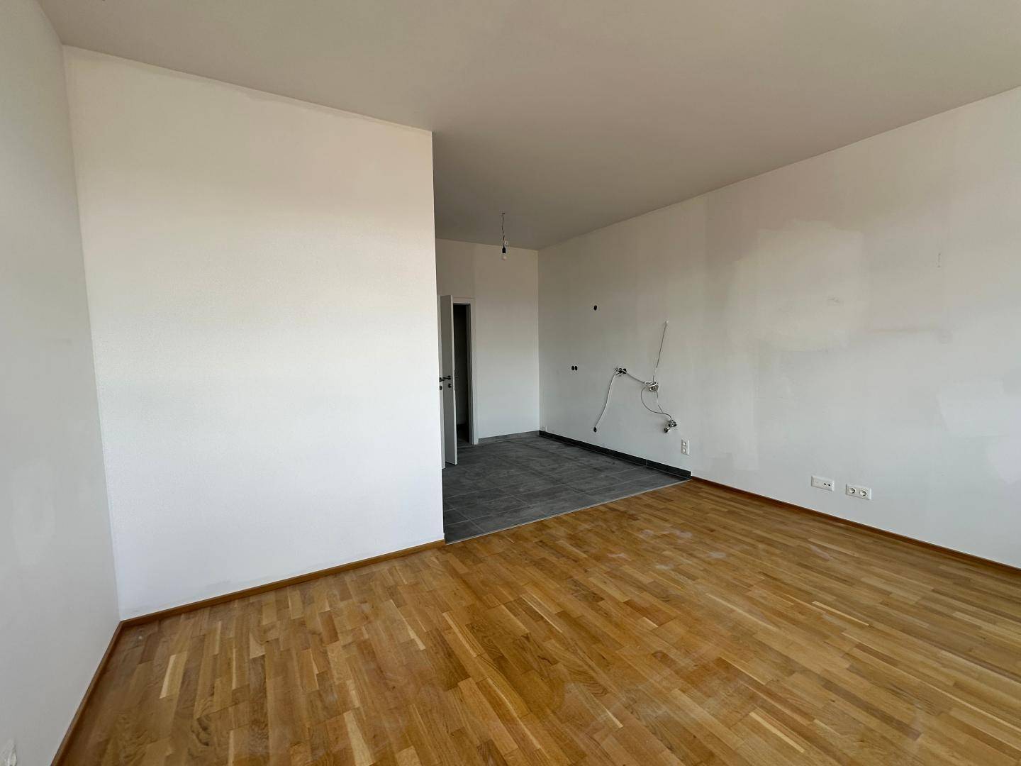 Geräumiger, leerer Wohnbereich mit Holzboden und einem gefliesten Eingangsbereich.