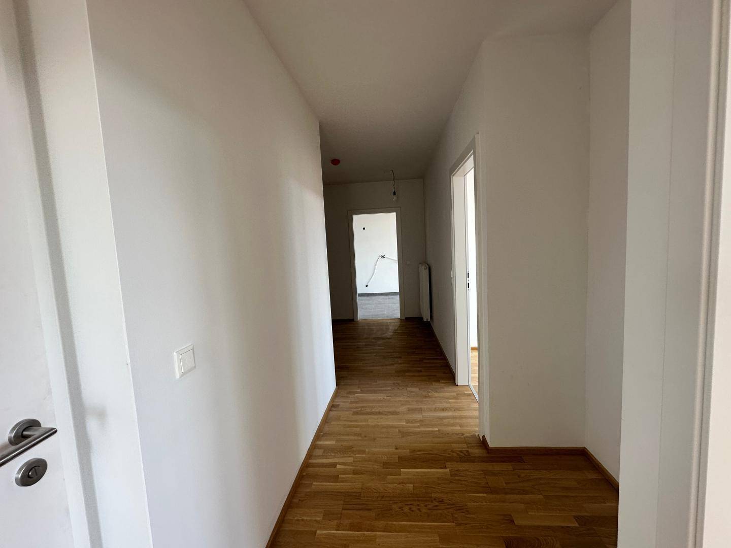 Langer, heller Flur mit Holzboden, der zu weiteren Räumen in der Wohnung führt.