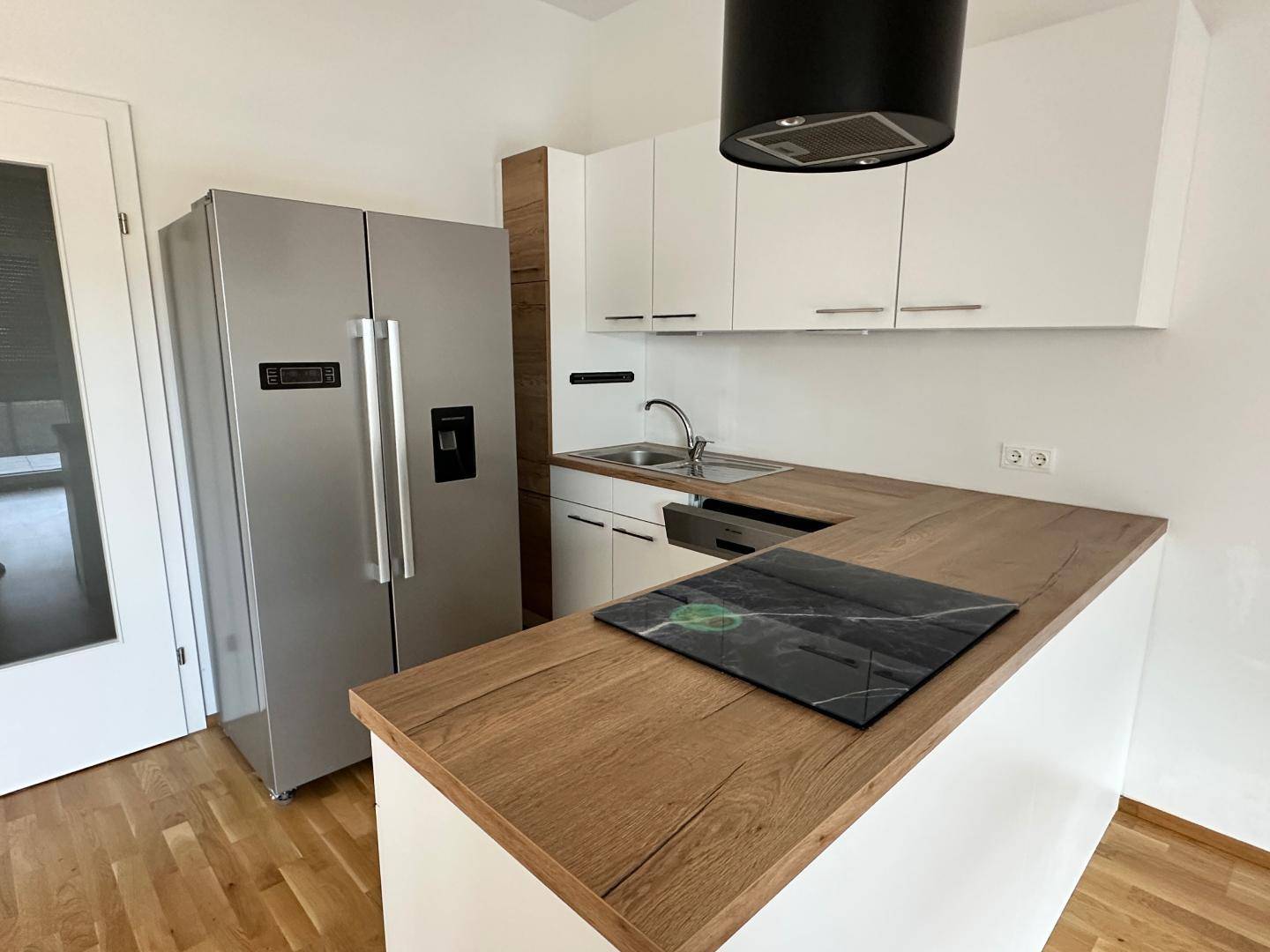 Kücheninsel mit modernem Induktionskochfeld und großem Kühlschrank in einer hellen Einbauküche.