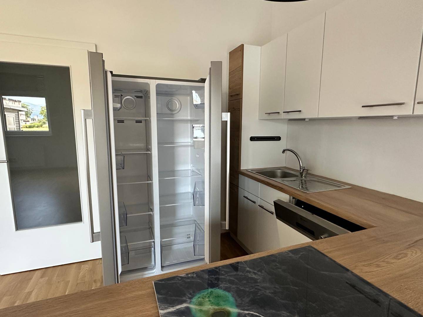 Offener Kühlschrank in einer modernen Küche mit weißer Front und Holz-Arbeitsplatte.
