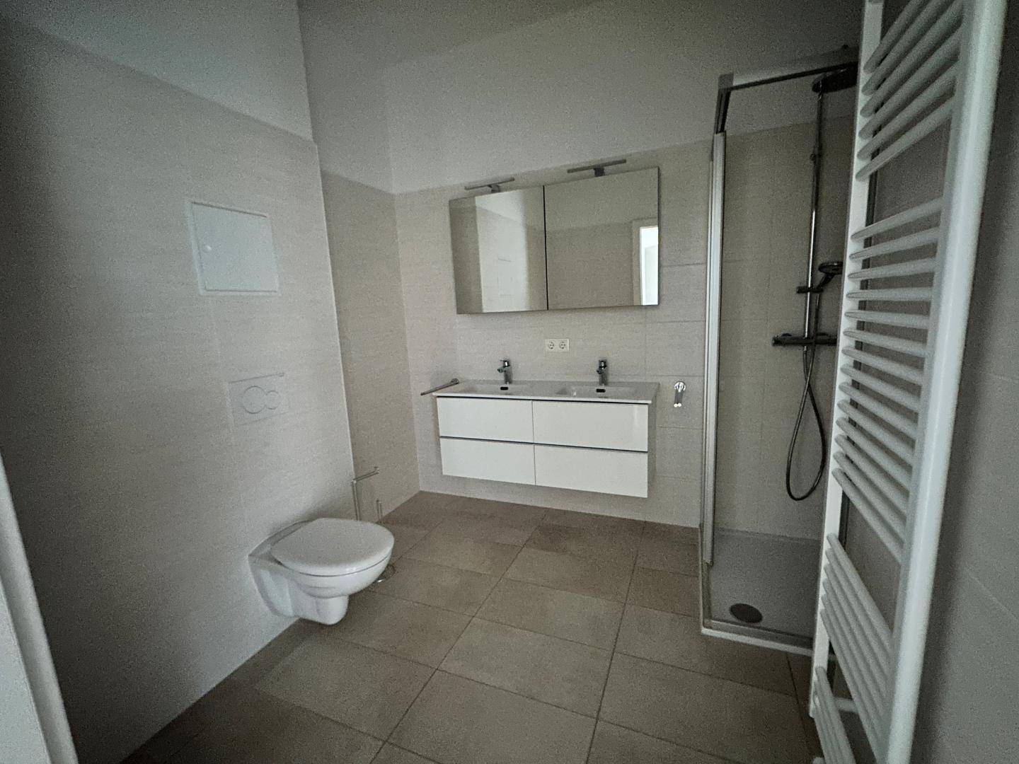 Modernes Badezimmer mit Doppelwaschbecken, Duschkabine, Wand-WC und beheiztem Handtuchhalter.