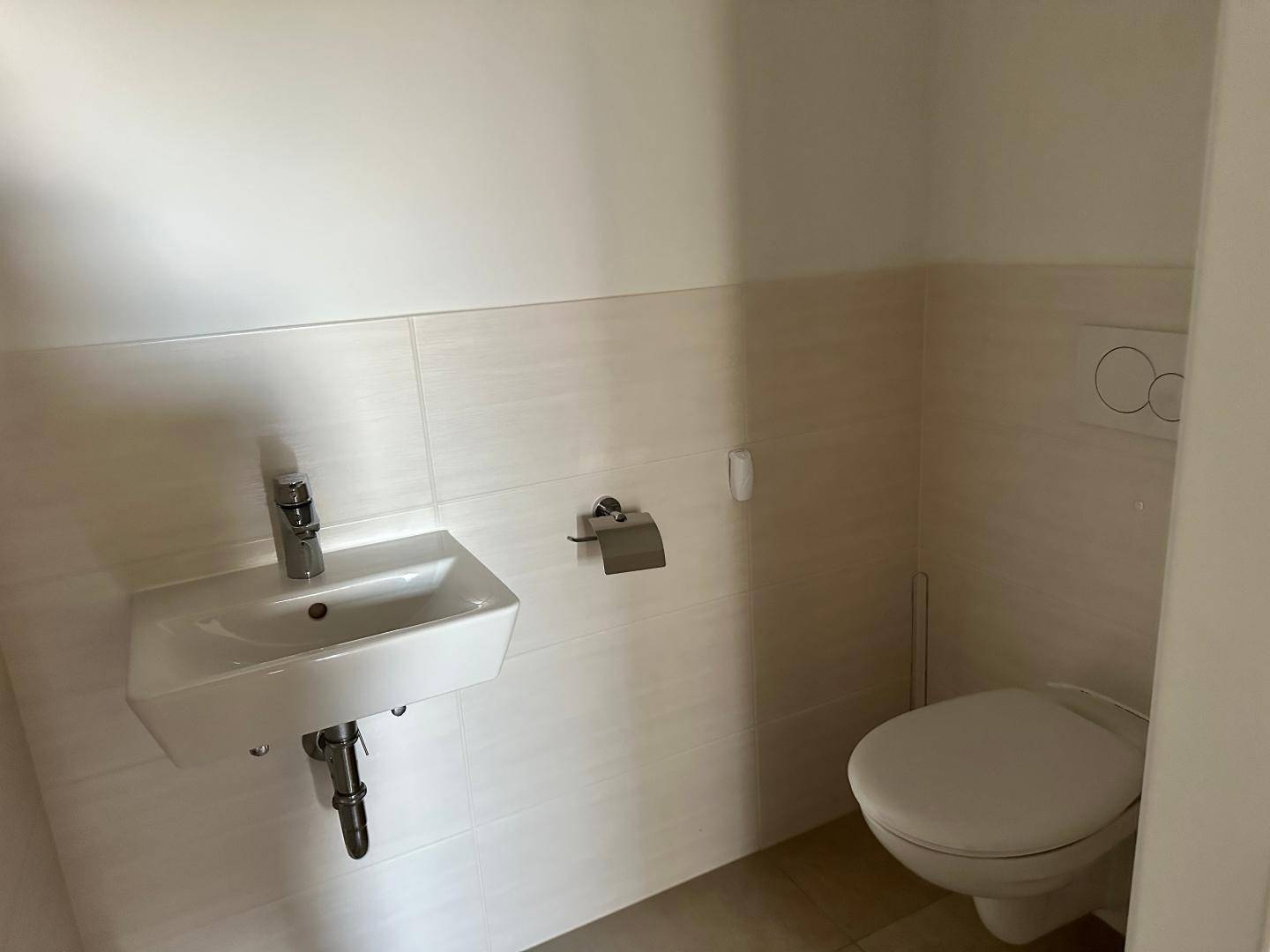 Gäste-WC mit kleinem Waschbecken und wandhängender Toilette, teilweise gefliest.