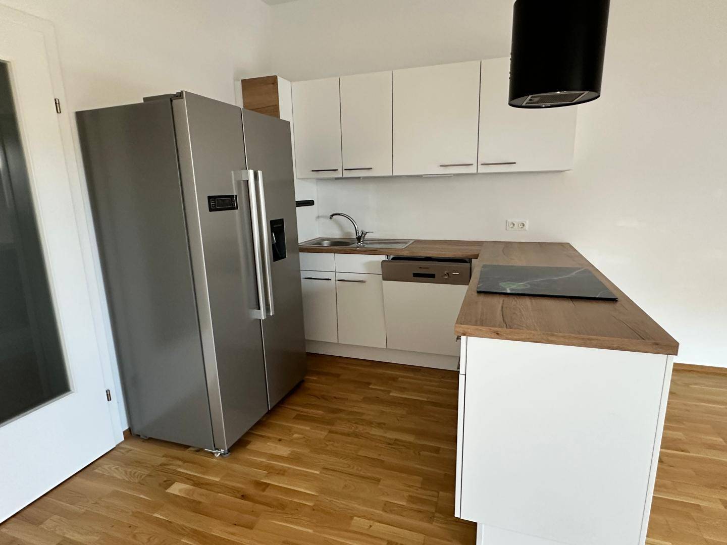 Detailansicht der modernen Küche mit weißer Front, Spüle, Geschirrspüler und großem Side-by-Side Kühlschrank.