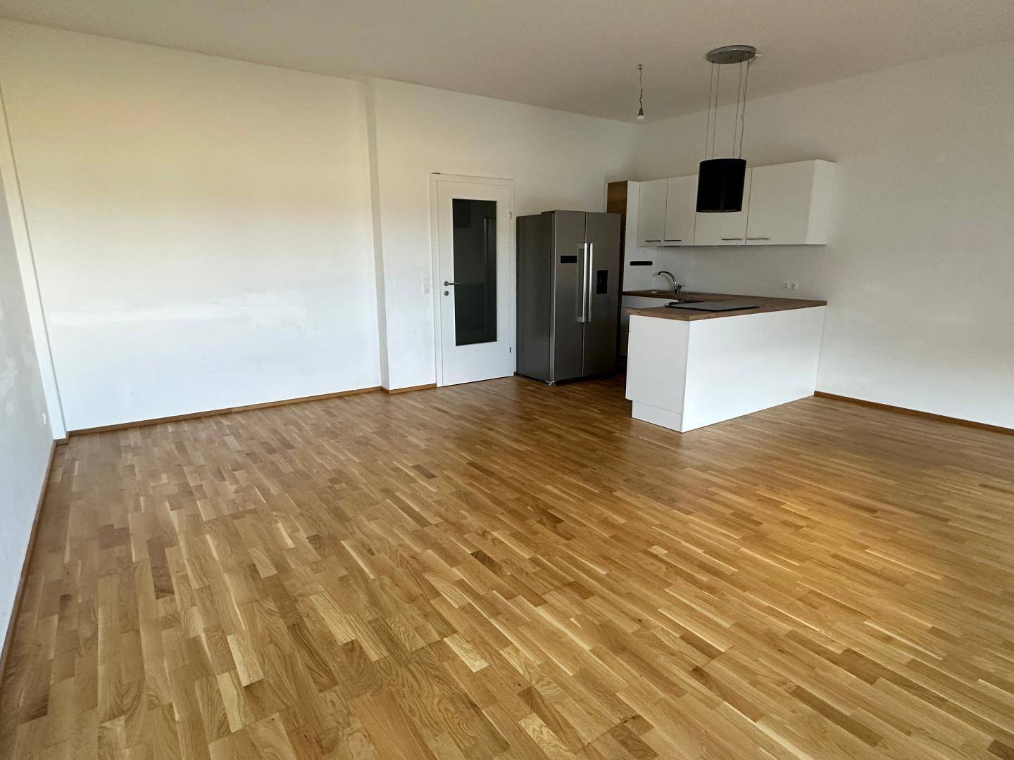 Geräumiger offener Wohnbereich mit integrierter Küche, Parkettboden und viel Tageslicht.