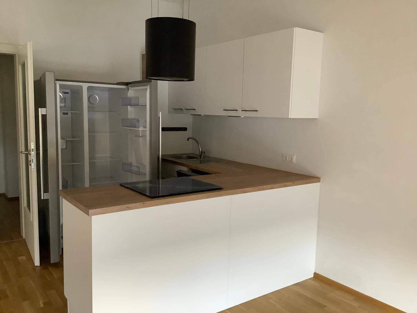 Moderne Küchenzeile mit weißer Front, Holz-Arbeitsplatte, Induktionskochfeld und großem Kühlschrank.