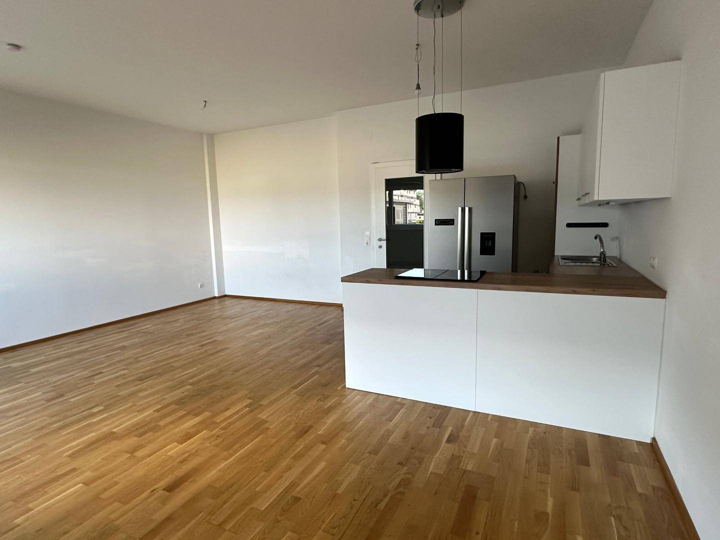 Heller Wohnbereich mit offener Küche, Parkettboden und moderner Pendelleuchte über der Kücheninsel.