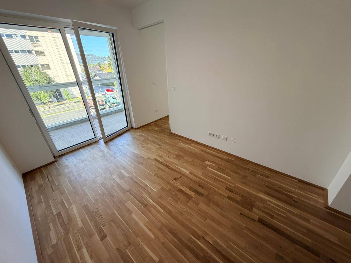 Heller Raum mit Holzboden und großen Schiebetüren, die zu einem Balkon führen.