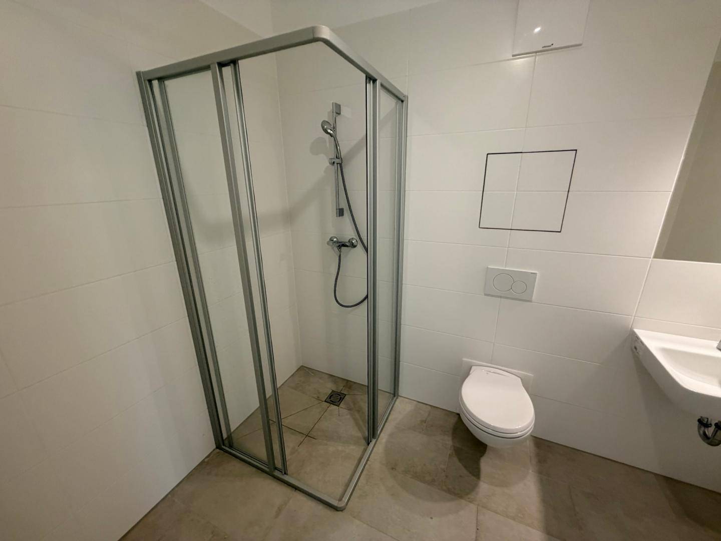 Zeitgemäßes Badezimmer mit Duschkabine, WC und Waschbecken, ausgestattet mit hellen Fliesen.