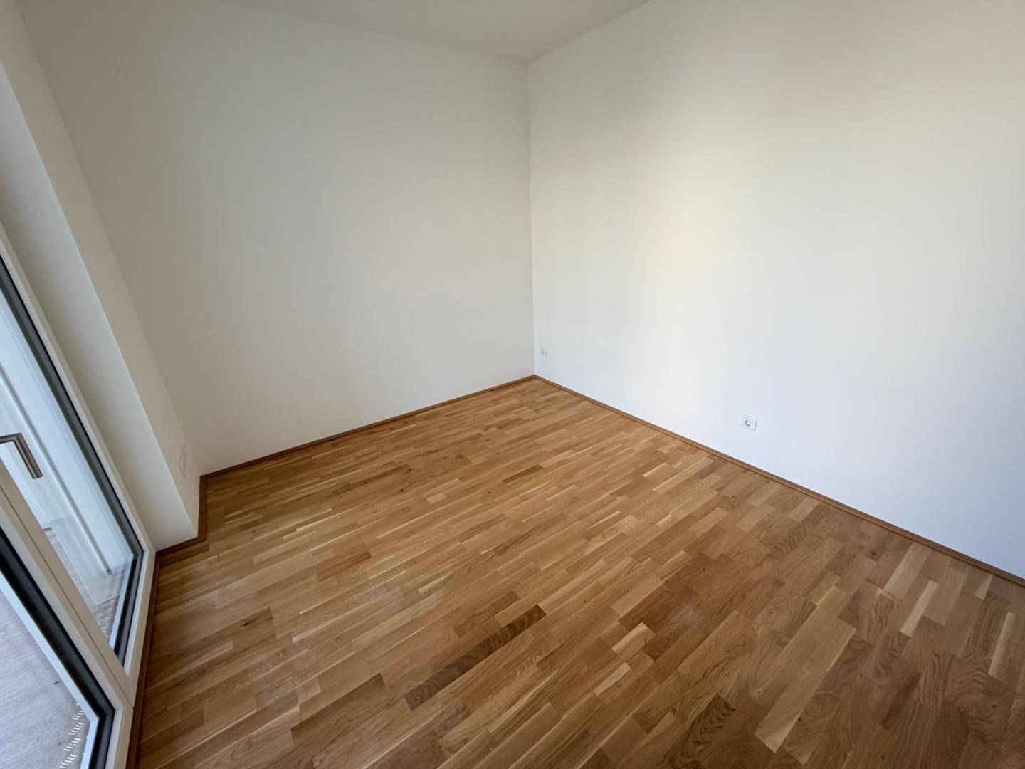 Helles Schlafzimmer mit Holzboden und Zugang zu einem Außenbereich durch eine Fenstertür.