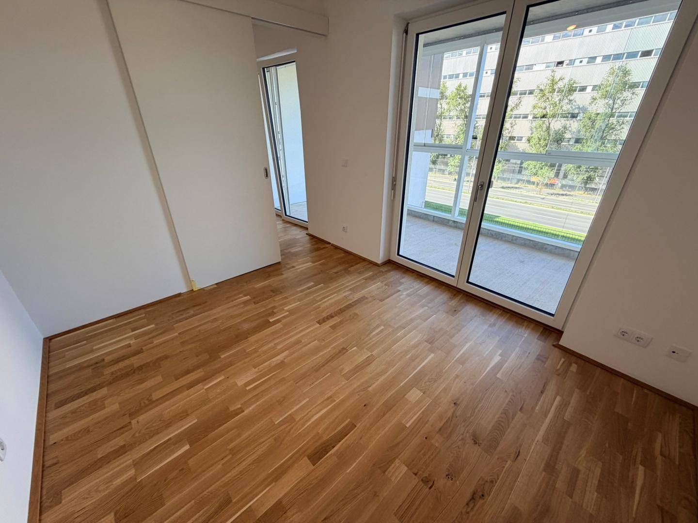 Geräumiger Raum mit Holzboden und großen Fenstern, die viel Tageslicht hereinlassen.