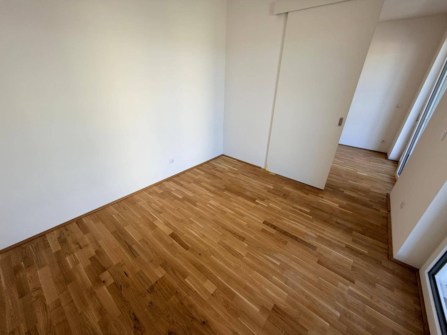 Helles Zimmer mit Holzboden und einer modernen Schiebetür, die zu einem weiteren Raum führt.