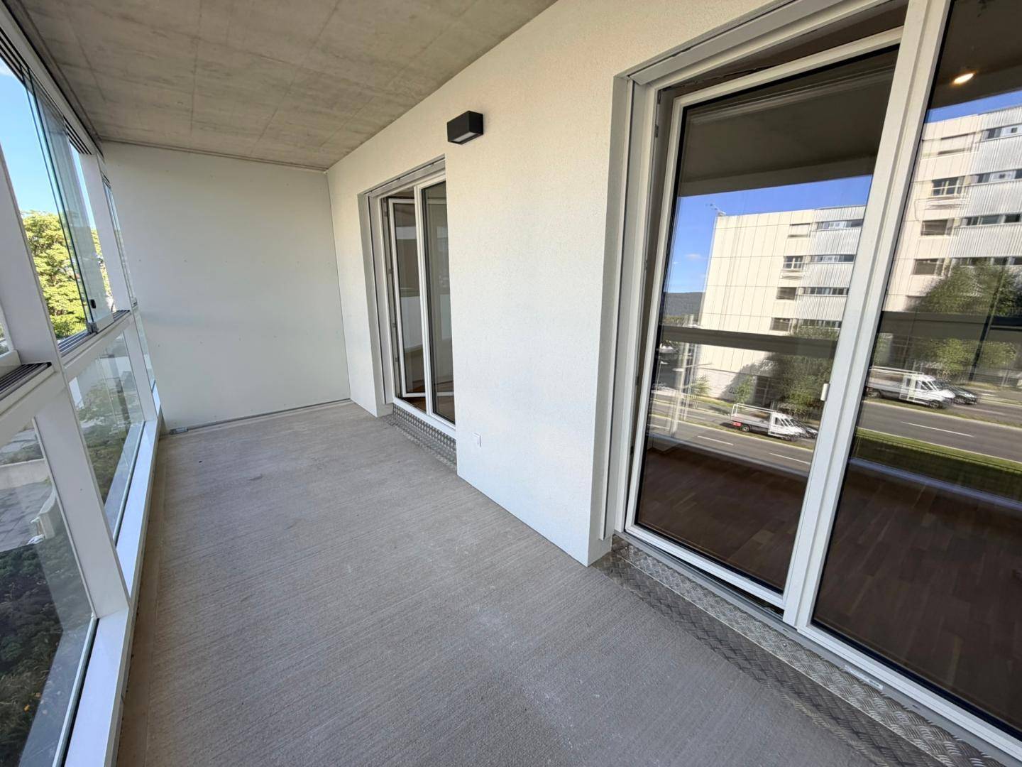 Geräumige Loggia mit Betonboden und Glasbrüstung, bietet einen Blick auf die Umgebung.