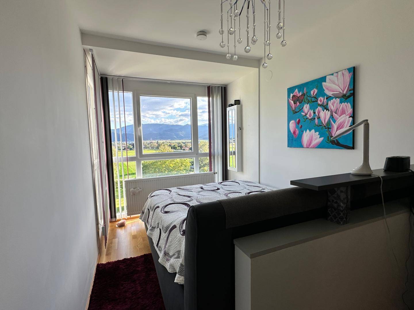 Schlafzimmer mit großem Fenster, Bergblick und modernem Kronleuchter.