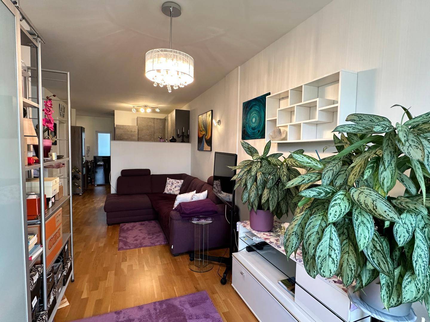 Geräumiges Wohnzimmer mit vielen Pflanzen, Holzboden und modernem Kronleuchter.