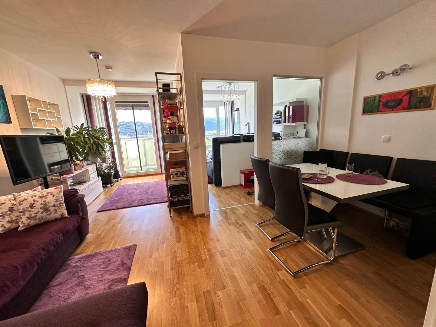 Kombinierter Wohn- und Essbereich mit Holzboden und Zugang zum Balkon.