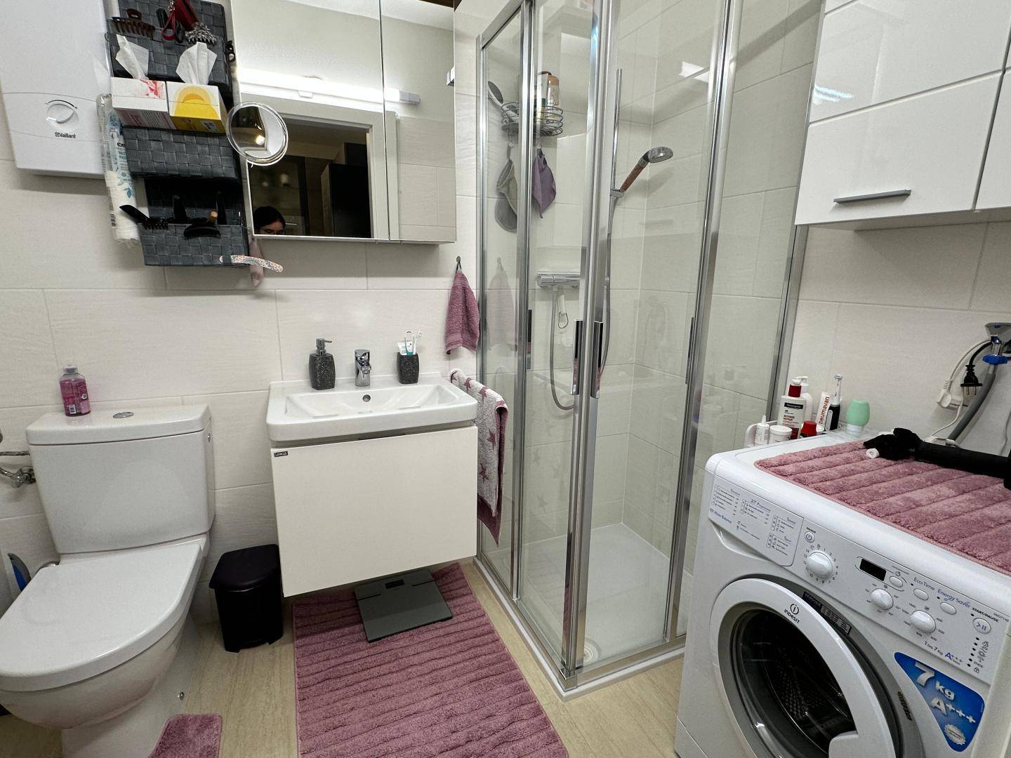 Badezimmer mit Duschkabine, Waschbecken, WC und Waschmaschine.
