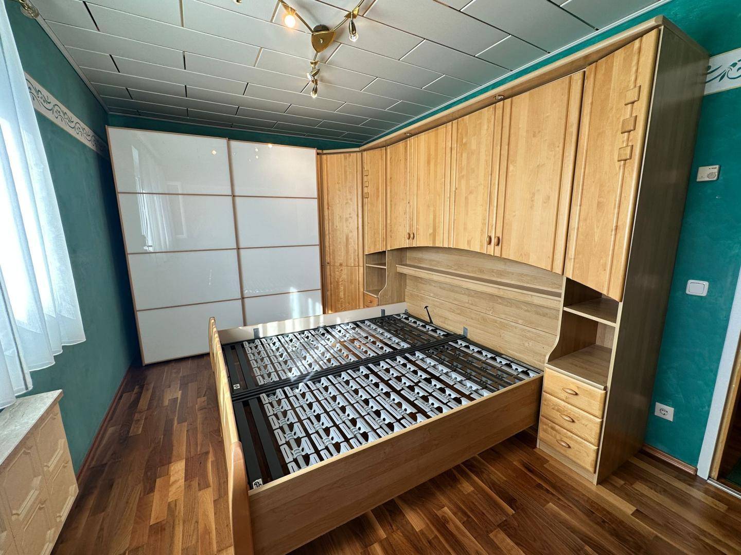 Schlafzimmer mit Holzboden, Einbauschränken und einem Bettgestell aus hellem Holz.