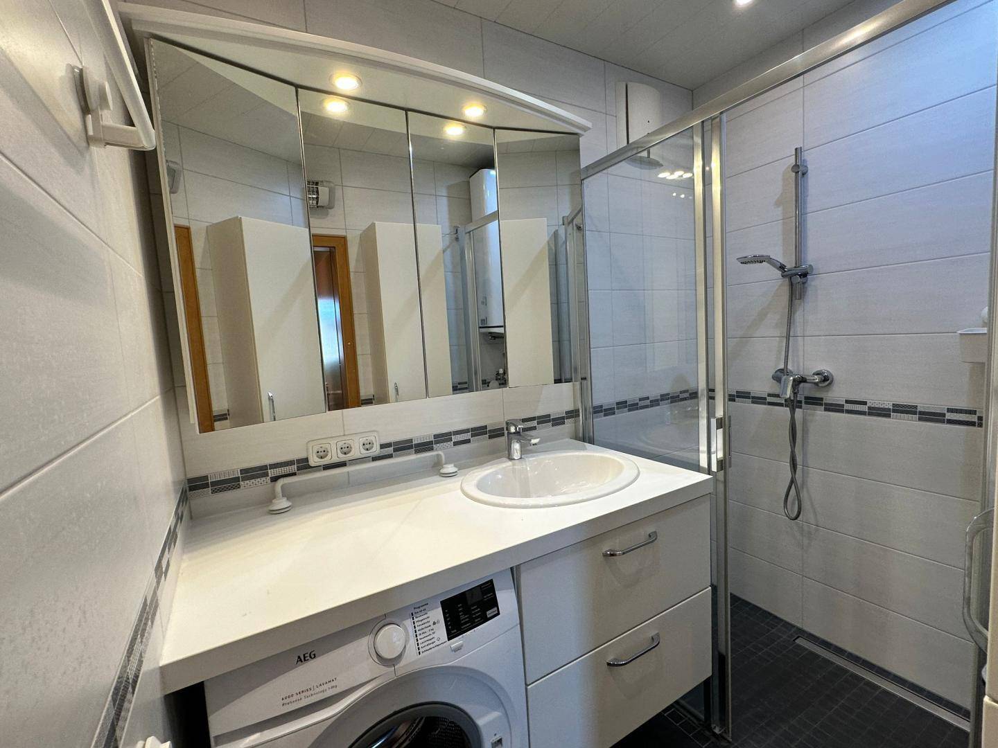 Modernes Badezimmer mit Dusche, Waschbecken und integrierter Waschmaschine unter der Arbeitsplatte.