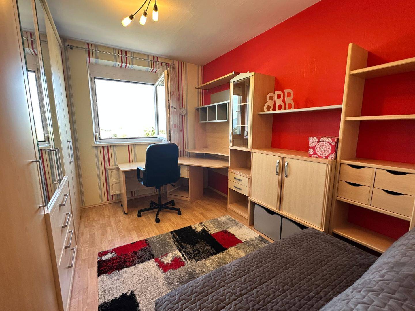Arbeitszimmer mit roter Wand, Schreibtisch und Regalen, ideal für ein Home-Office.