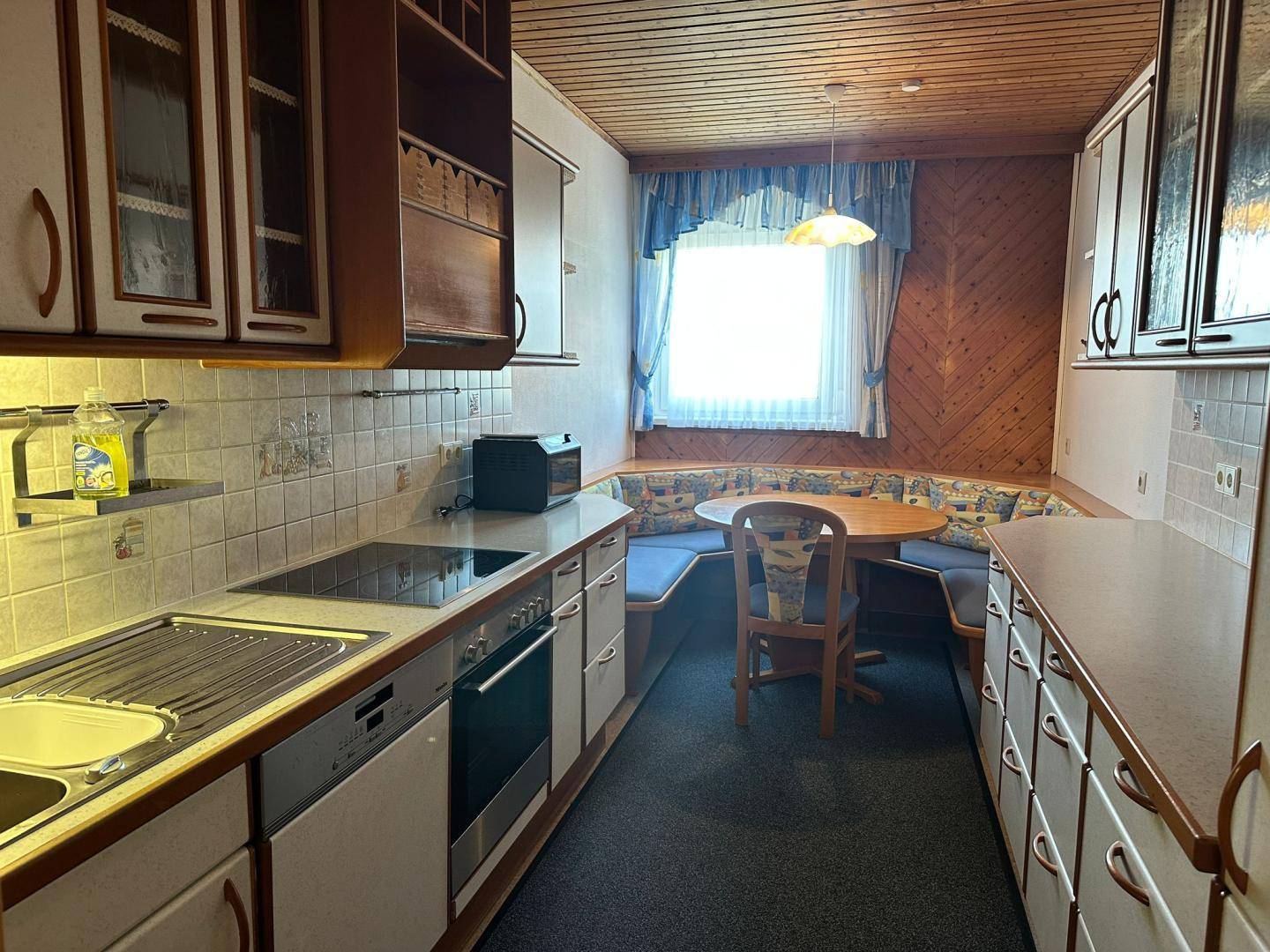Funktionale Küche mit Einbaugeräten, Essbereich und Holzvertäfelung an den Wänden und Decke.