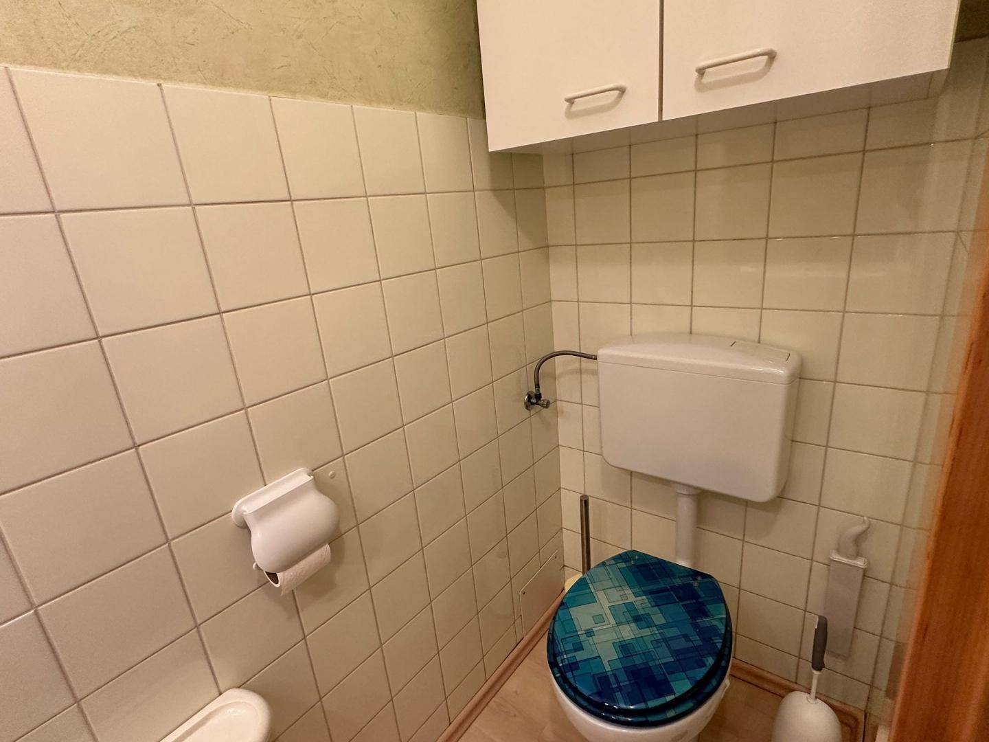 Gäste-WC mit Toilette und weißen Fliesen, ausgestattet mit einem farbigen Toilettensitz.