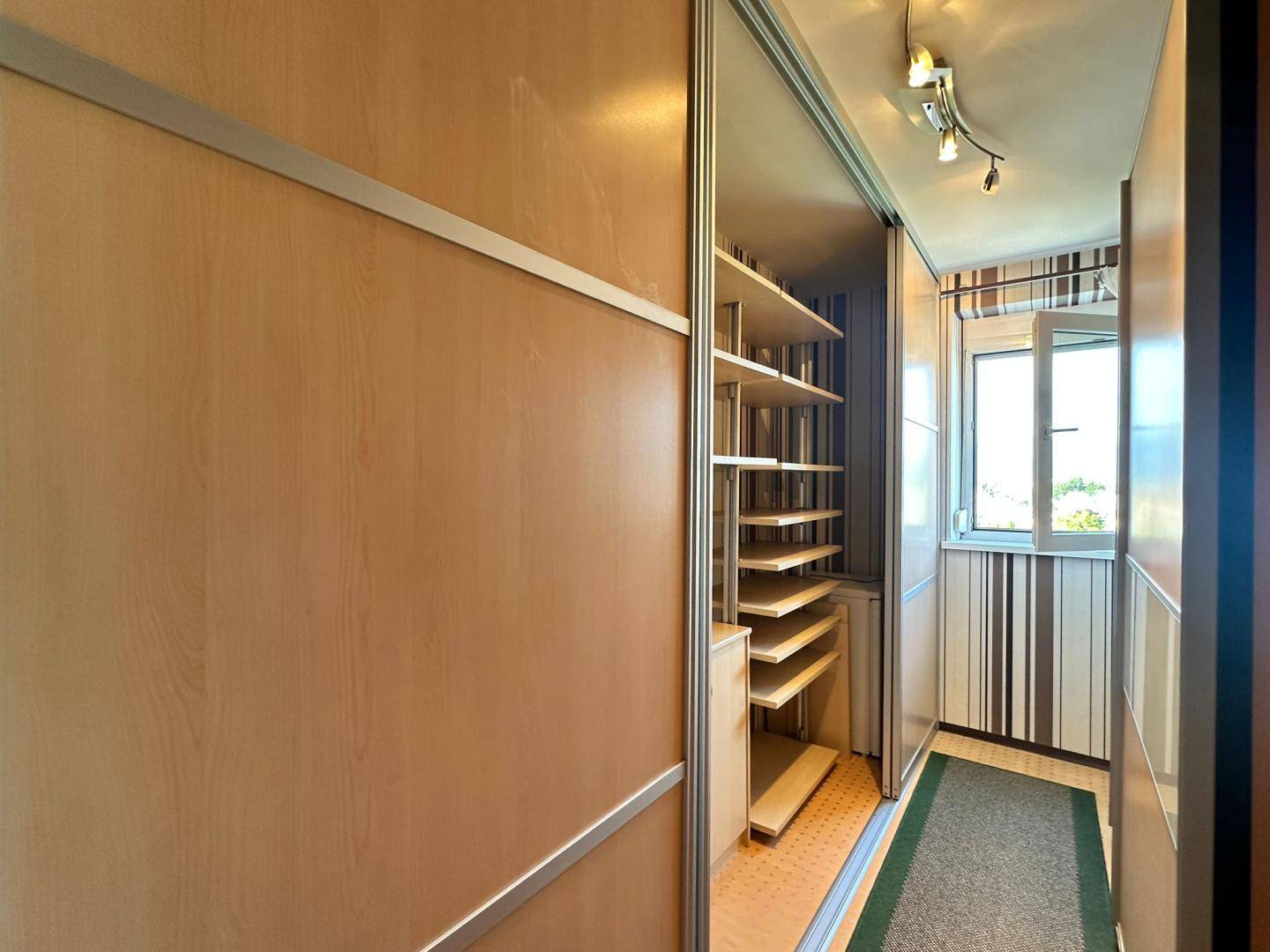 Flur mit integrierten Regalen hinter Schiebetüren und Zugang zum verglasten Balkon.