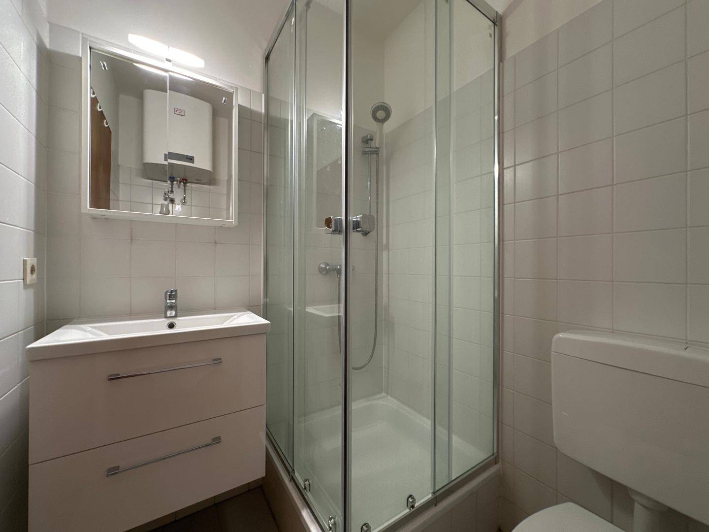 Kleines Badezimmer mit Duschkabine, Waschbecken und WC, ausgestattet mit weißen Fliesen.