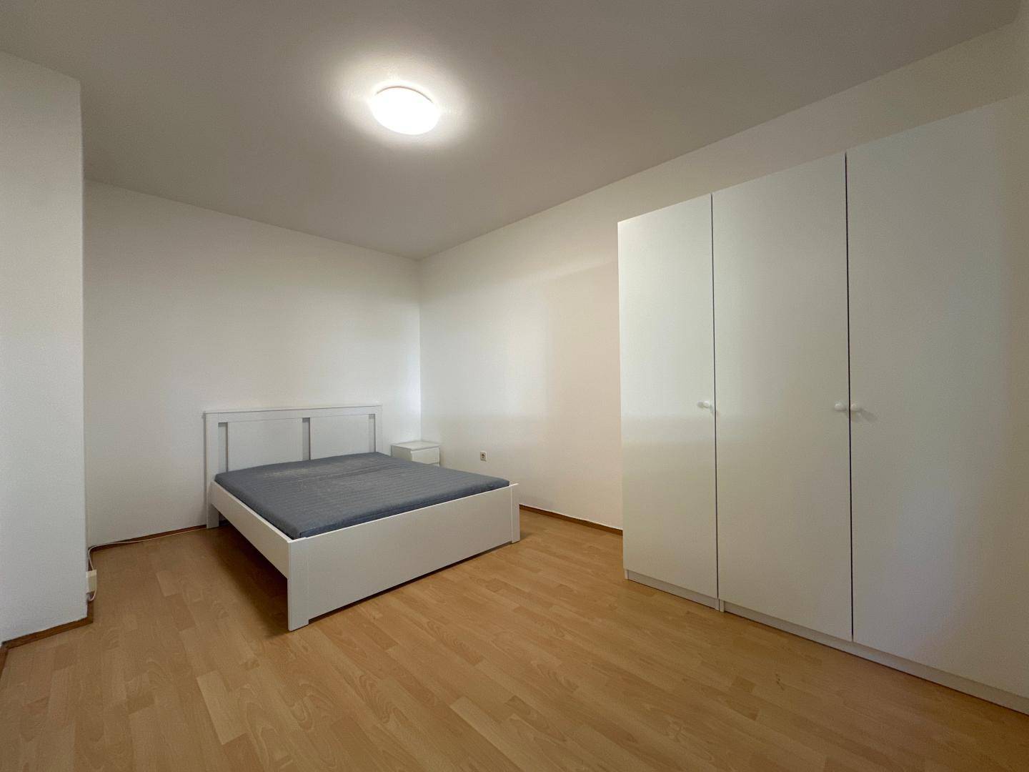 Helles Schlafzimmer mit weißem Bettrahmen, großem Kleiderschrank und hellem Parkettboden.