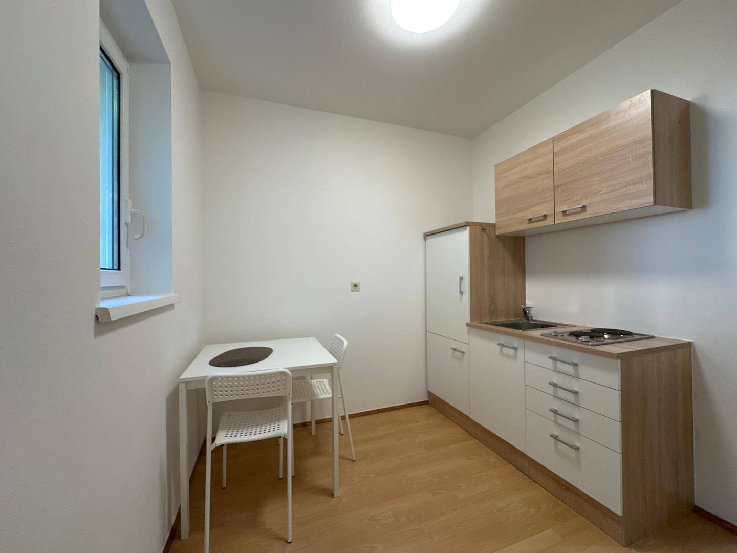 Funktionale Küchenzeile mit hellen Holzfronten, integriertem Kühlschrank und kleinem Essbereich am Fenster.