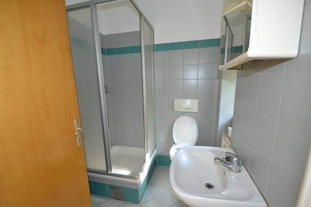 Badezimmer mit Duschkabine, Toilette und Waschbecken, gefliest in Grau und Türkis.