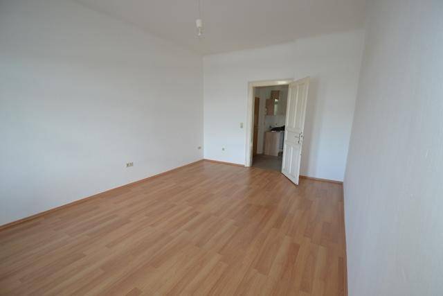 Leerer Wohnraum mit hellem Laminatboden und Zugang zu einem weiteren Zimmer.