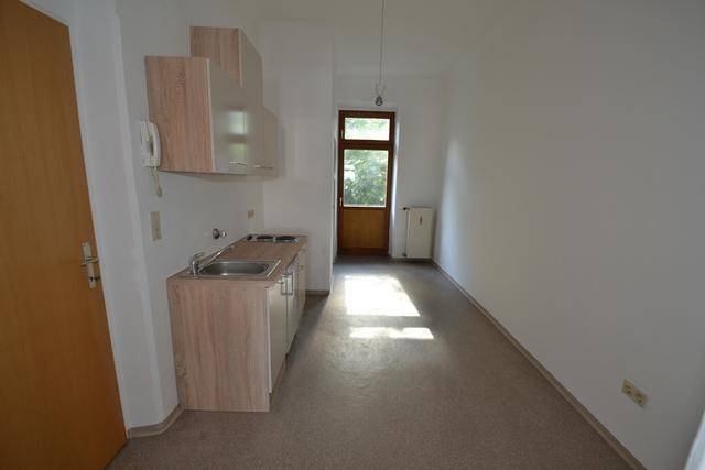 Kleine Einbauküche mit Spüle und Kochfeld in einem hellen Raum mit Zugang zum Balkon.