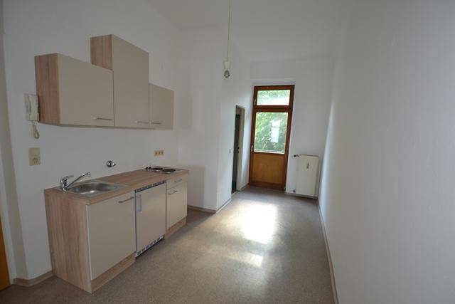 Kleine Einbauküche mit Spüle und Kochfeld in einem hellen Raum mit Zugang zum Balkon.