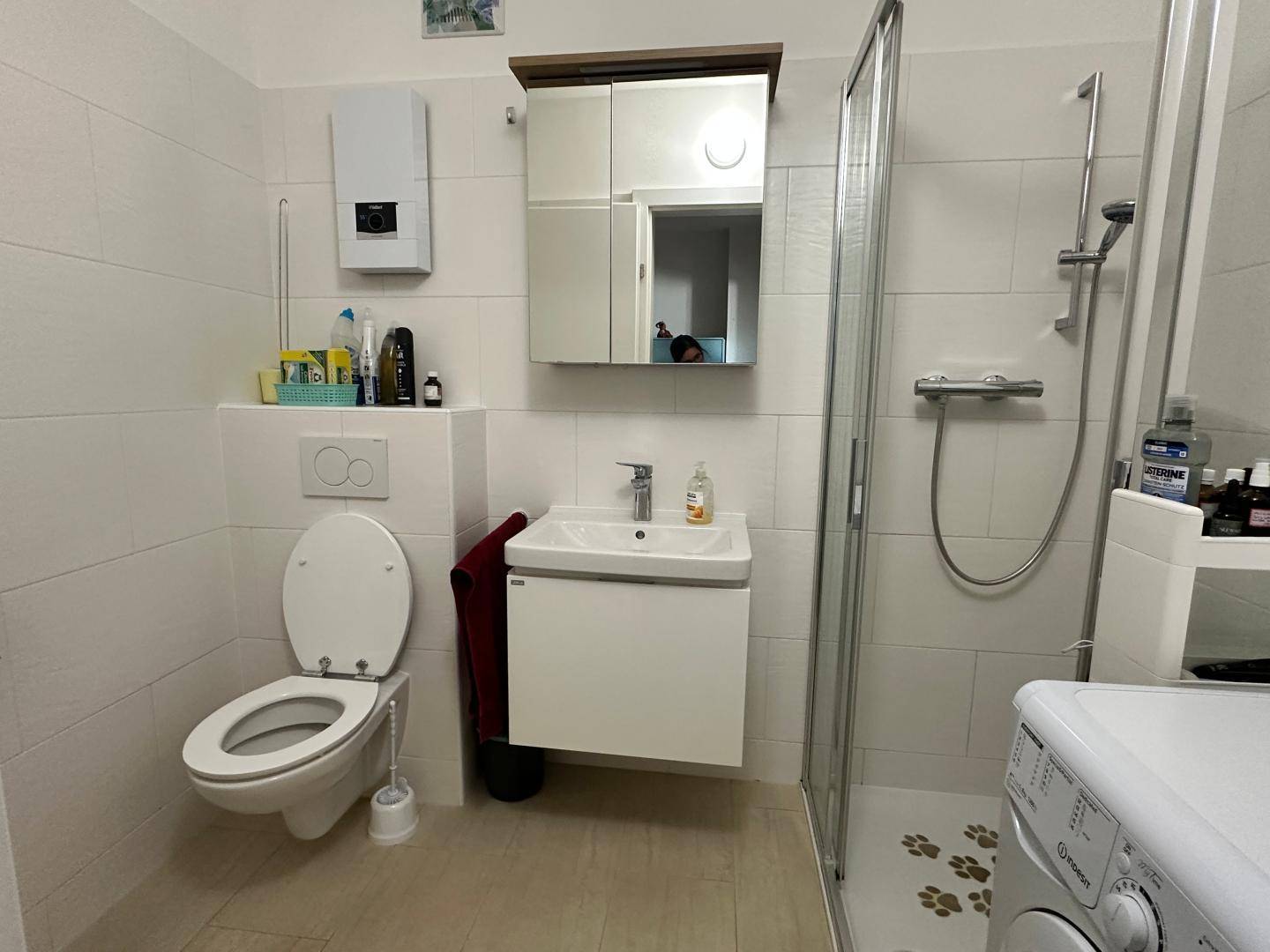 Helles Badezimmer mit WC, Waschbecken, Dusche und weiß gefliesten Wänden.