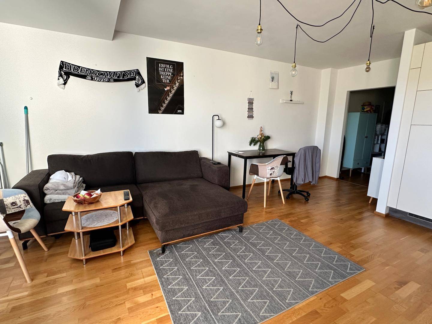 Gemütliches Wohnzimmer mit Sofa, Parkettboden und moderner Deckenbeleuchtung.