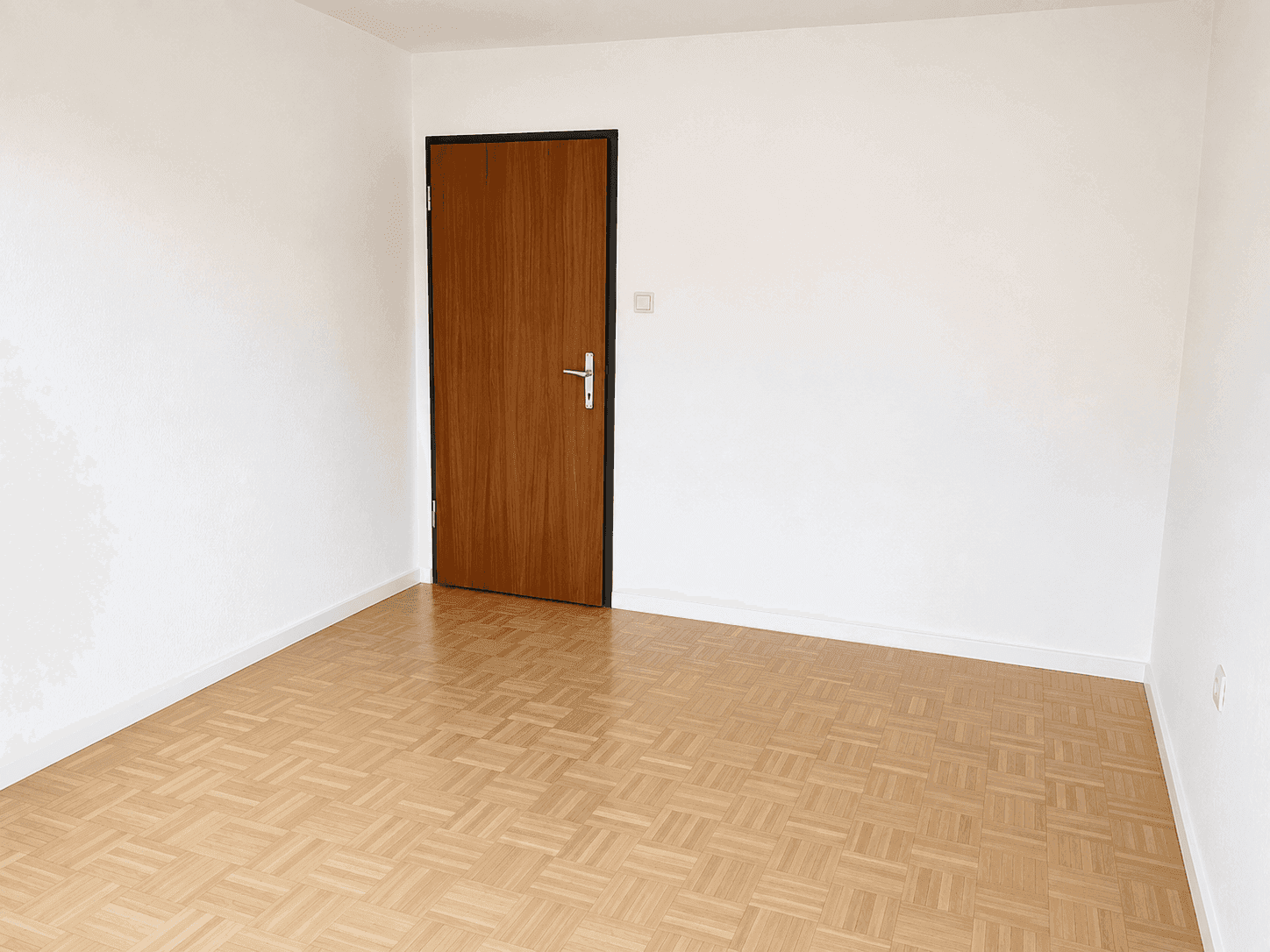 Leerer Raum mit hellem Parkettboden und weiß gestrichenen Wänden.