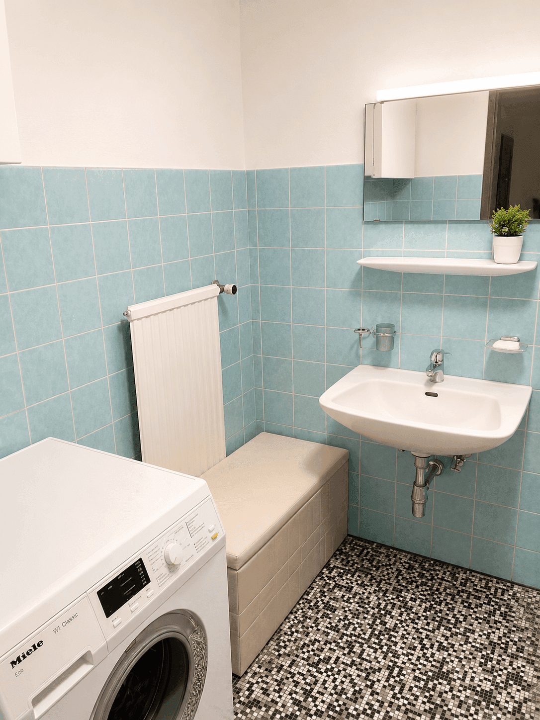 Badezimmer mit blauen Fliesen, Waschbecken, Spiegel und Waschmaschine.