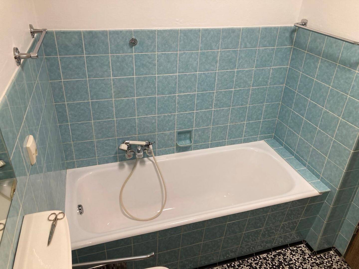 Badezimmer mit blauen Fliesen und einer Badewanne mit Duscharmatur.