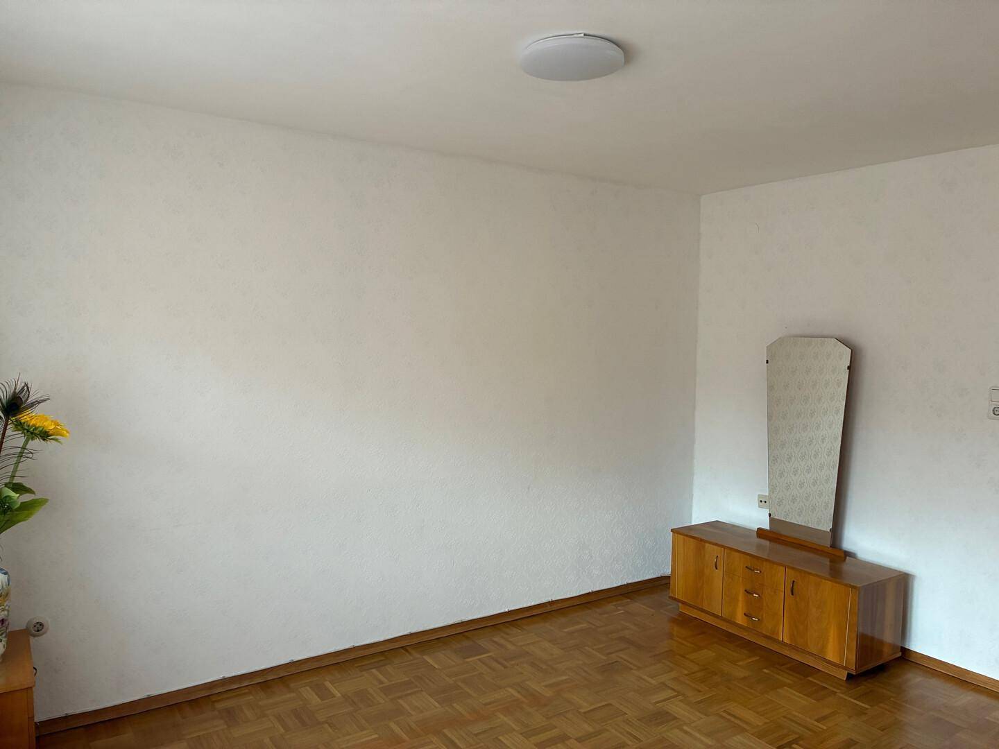 Heller Raum mit Parkettboden und einem Sideboard mit Spiegel.
