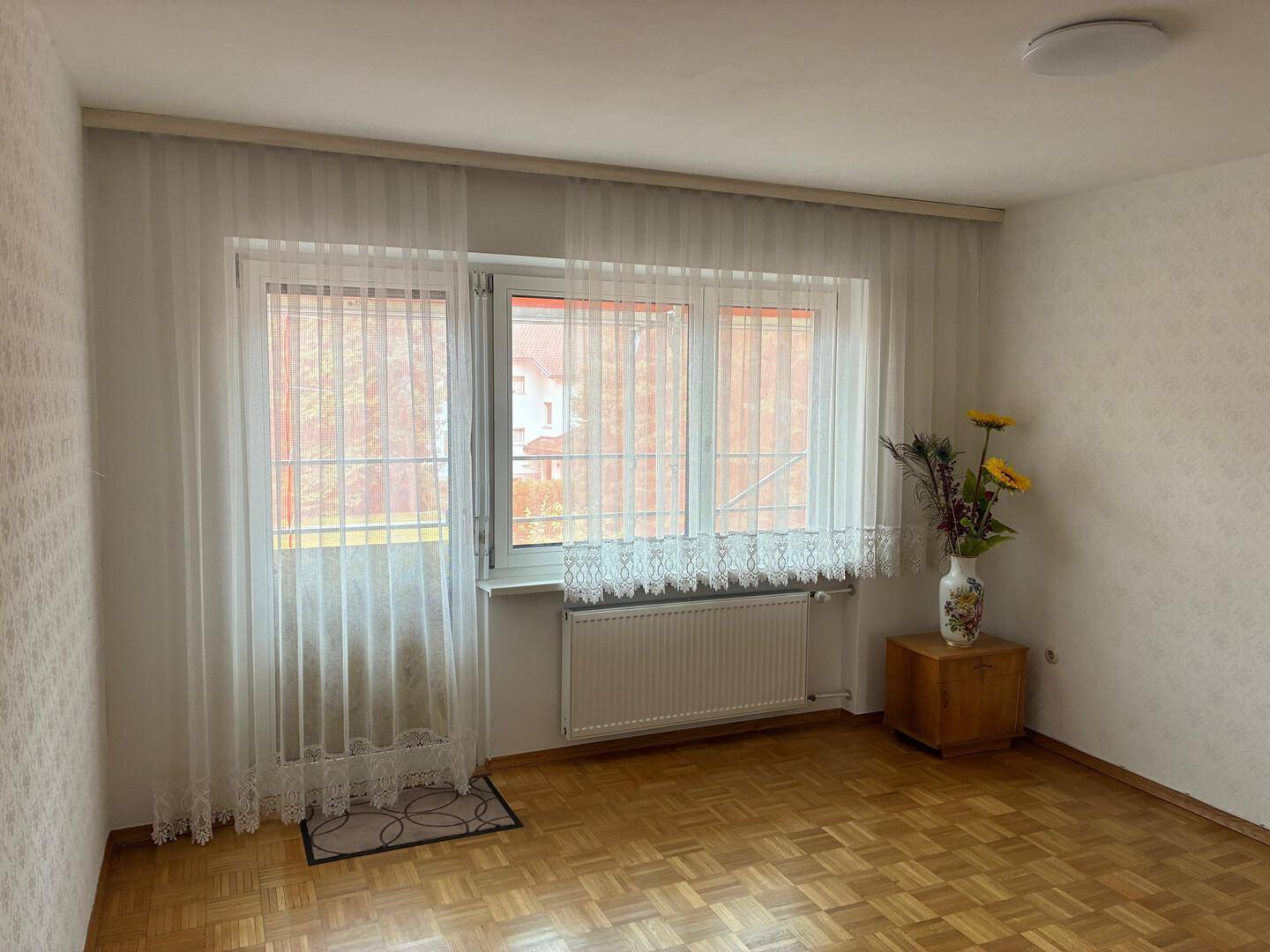 Heller Raum mit Parkettboden, großem Fenster und Vorhängen.