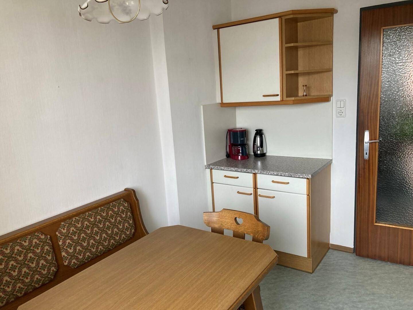 Gemütlicher Essbereich mit Holztisch, Eckbank und kleiner Küchenzeile.
