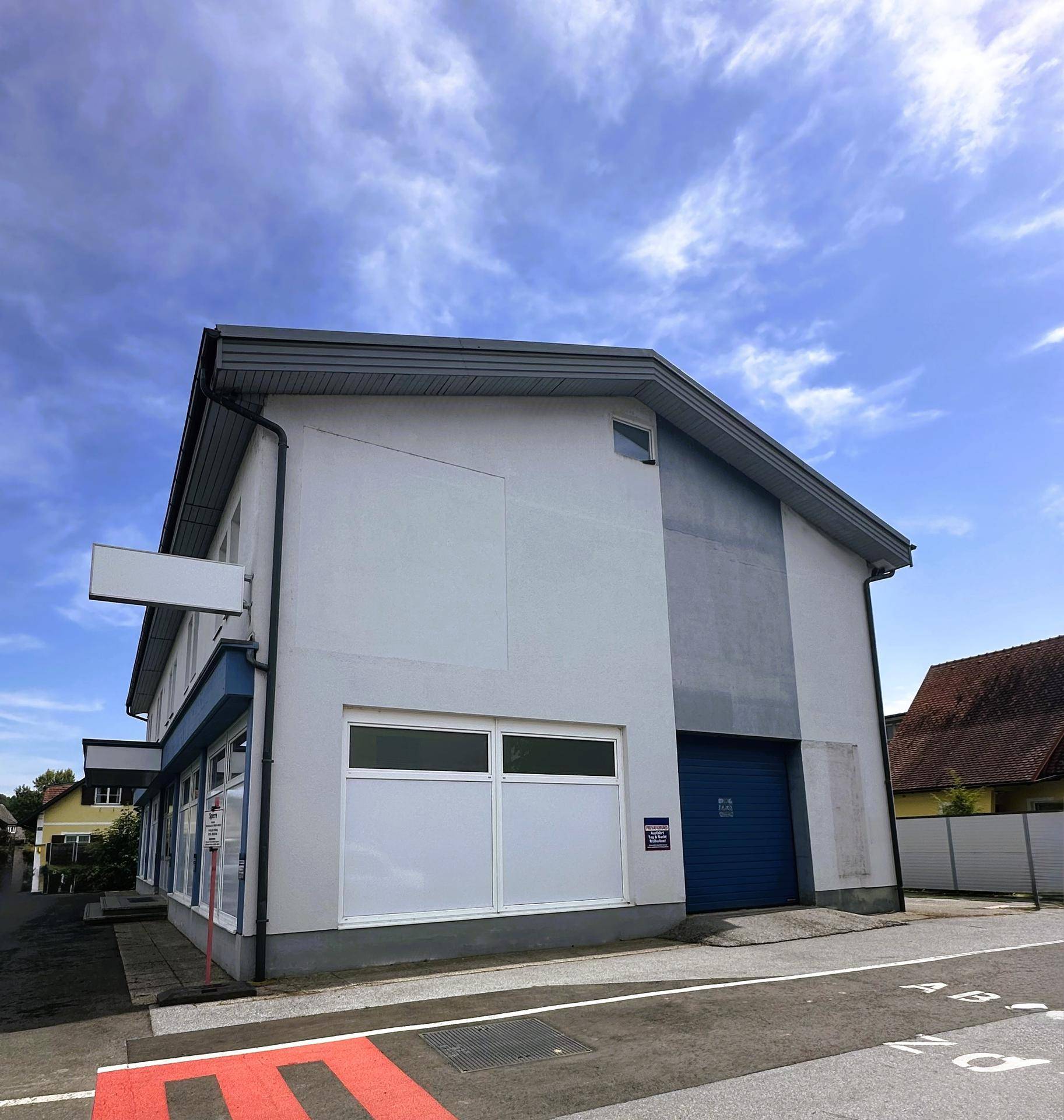 Seitenansicht des Geschäftsgebäudes mit blauer Rolltor und großen Fenstern unter einem bewölkten Himmel.