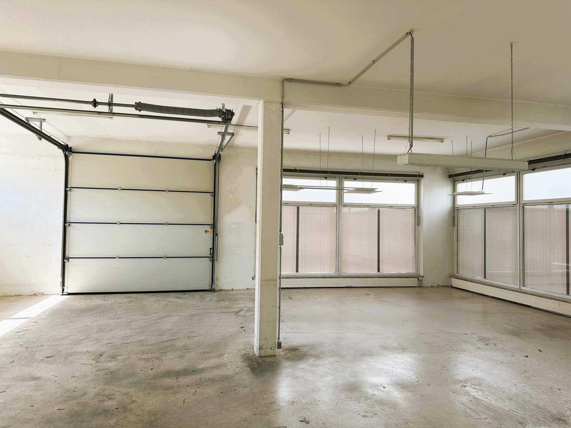 Geräumige Garage mit Betonboden, einem großen Rolltor und mehreren Fenstern für natürliche Belichtung.