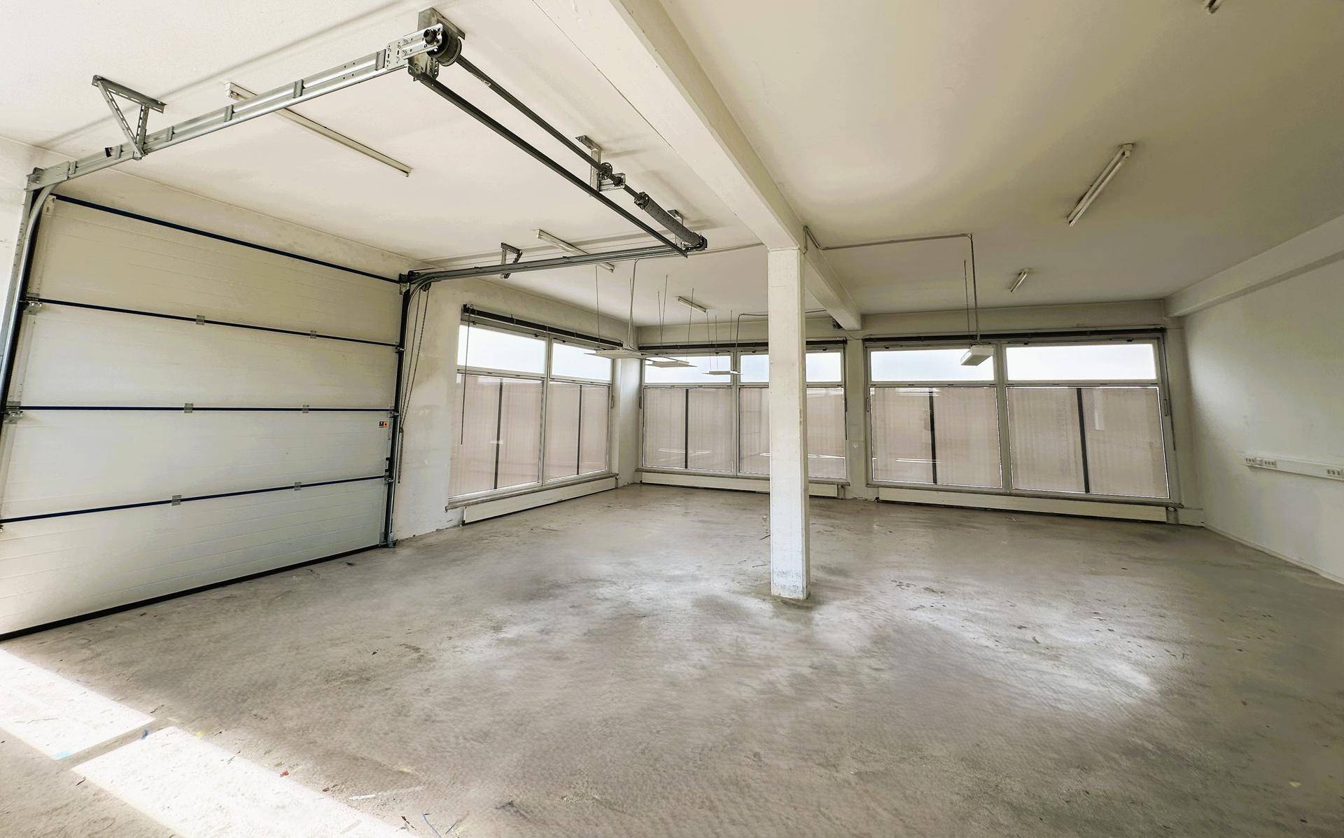 Große Garage oder Lagerhalle mit Betonboden, Rolltor und Fenstern, die Tageslicht hereinlassen.