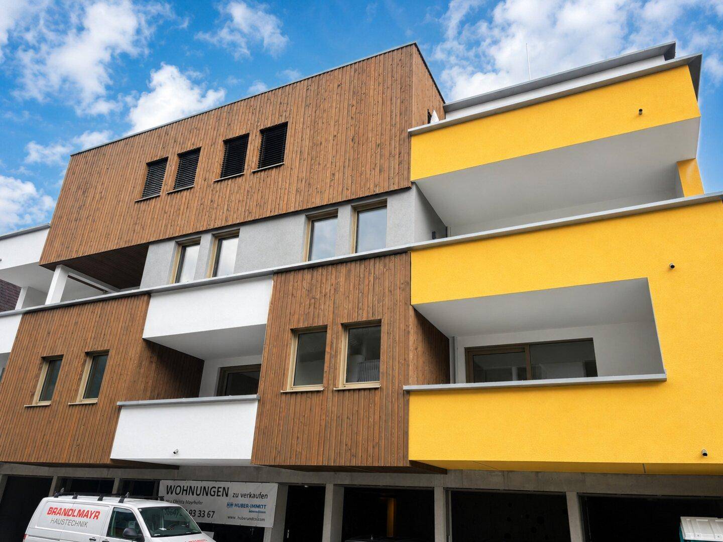 Moderne Architektur des Wohngebäudes mit Holzfassade, gelben Balkonen und großen Fenstern.