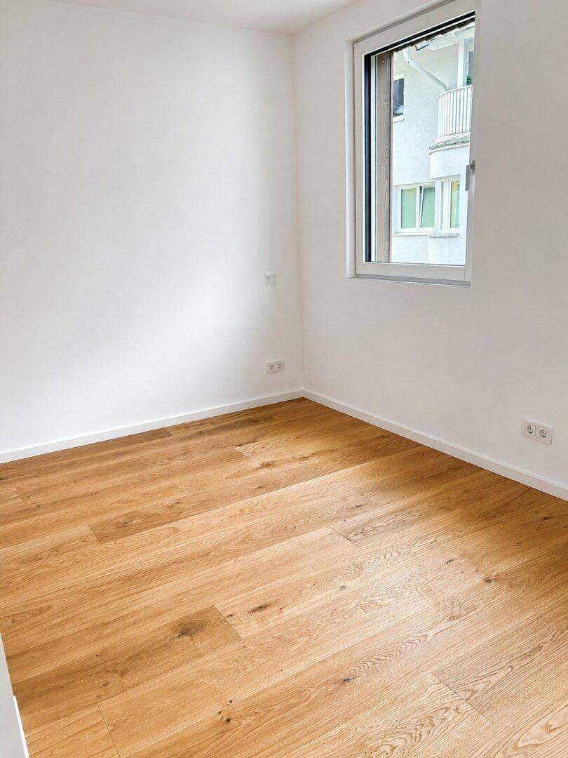 Helles Schlafzimmer mit Eichenparkett und einem Fenster mit Blick auf die Umgebung.