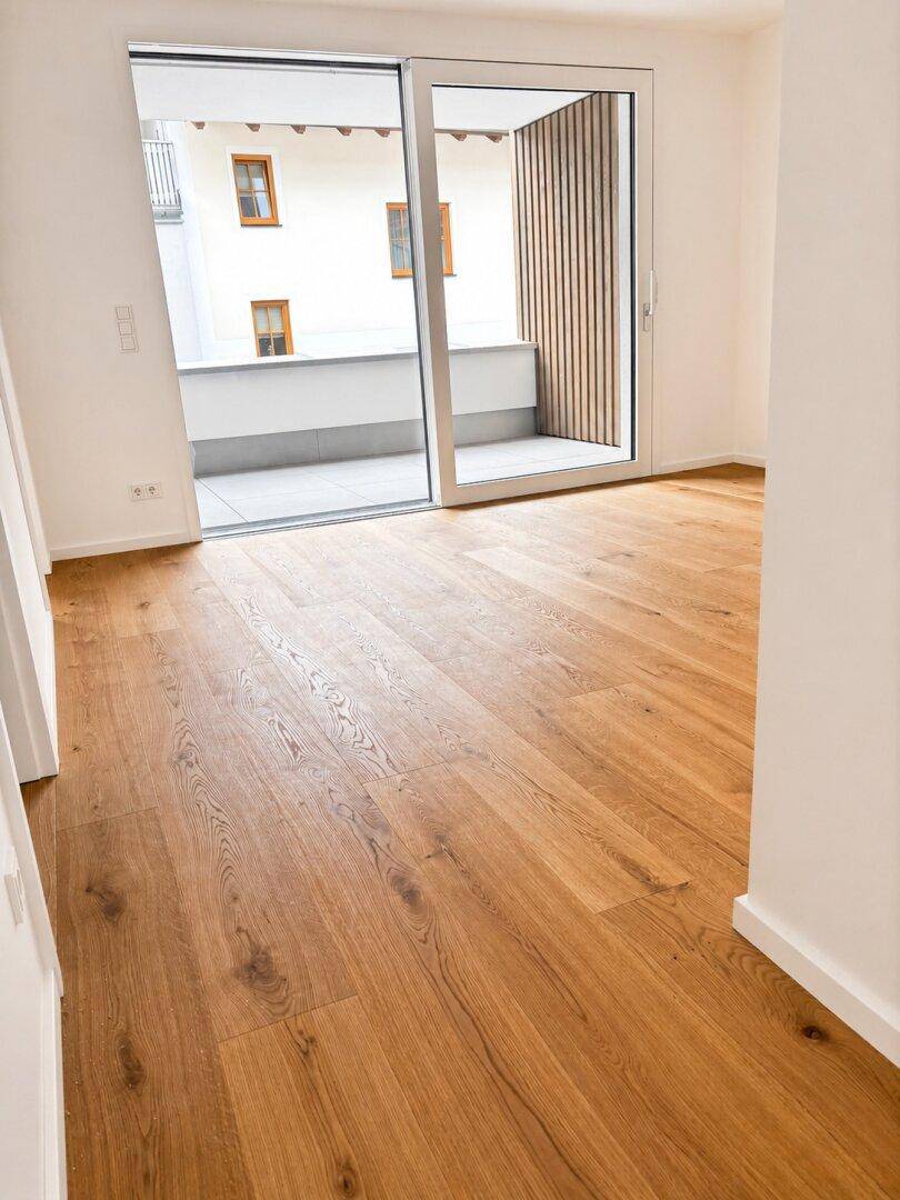 Heller Wohnraum mit Eichenparkett und großem Schiebefenster zum Balkon oder zur Loggia.