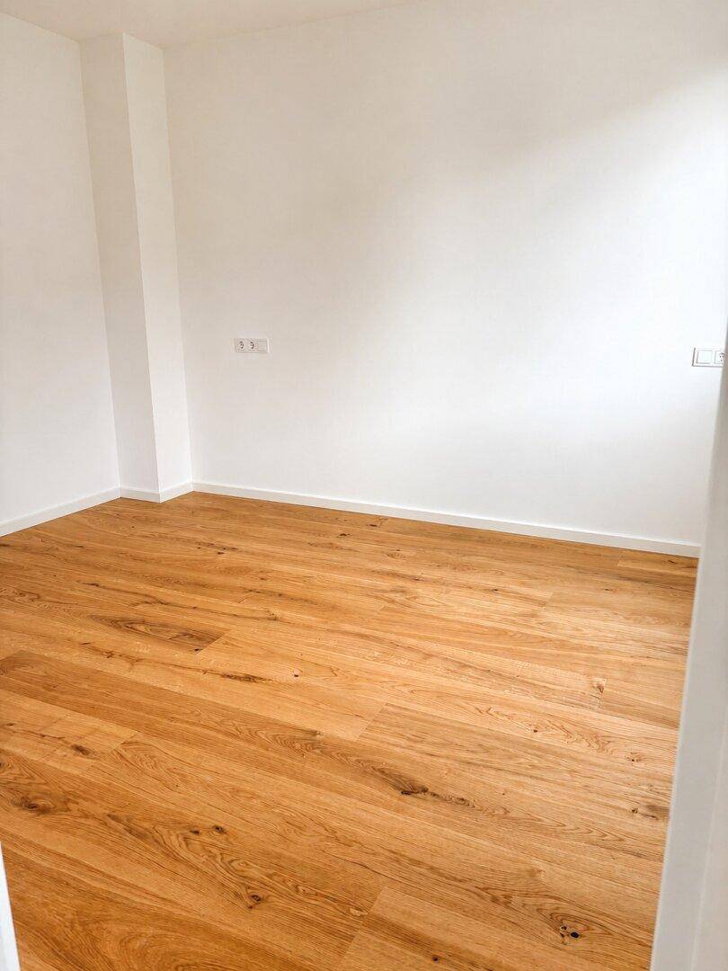 Leeres Schlafzimmer mit hellem Eichenparkett und weißen Wänden, bereit zur individuellen Gestaltung.