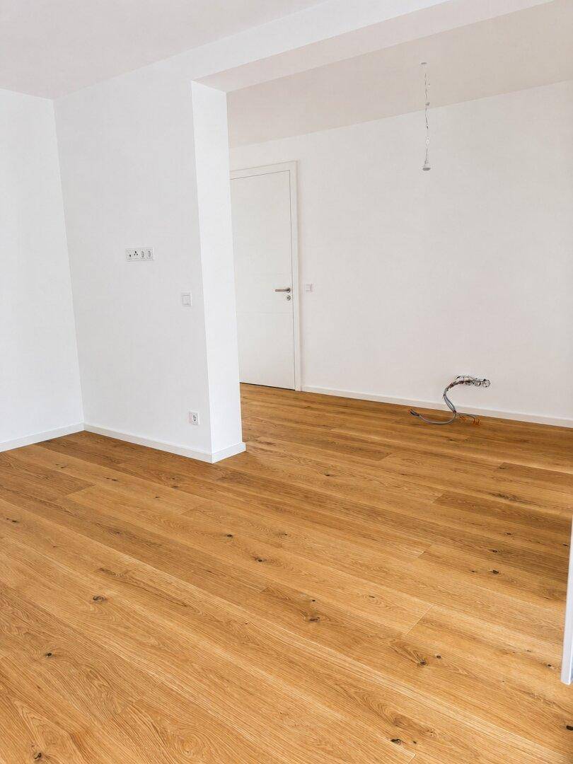 Geräumiges, unmöbliertes Wohnzimmer mit Eichenparkettboden und weißen Wänden.