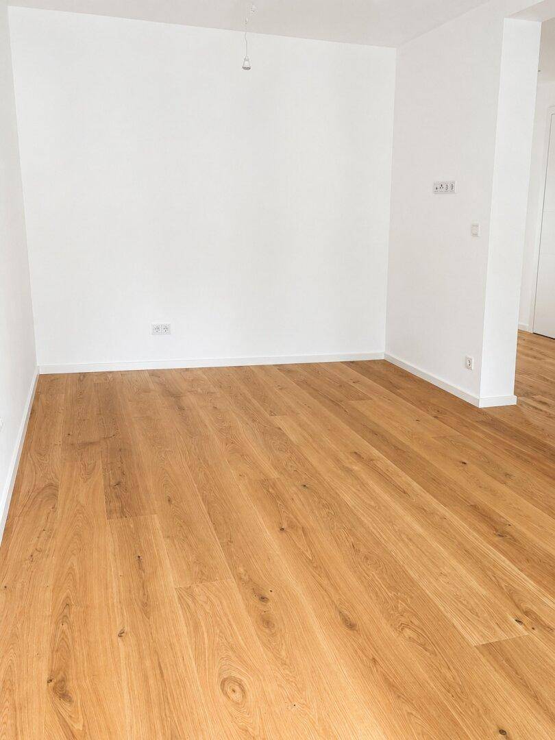 Helles, leeres Zimmer mit Eichenparkettboden und weißen Wänden, ideal für individuelle Gestaltung.
